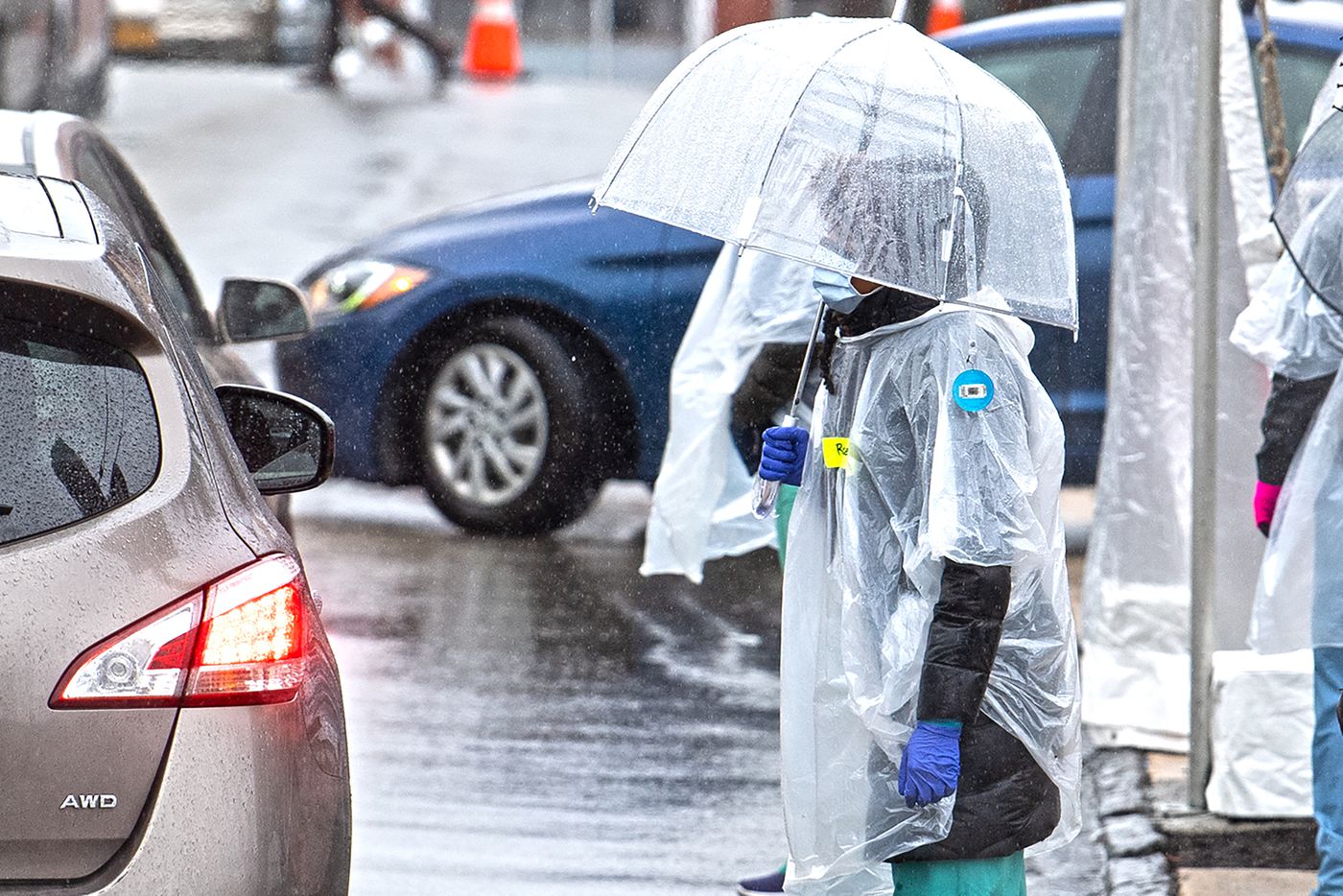 woman with a facemask stands at the edge of the street under a clear umbrella in the rain