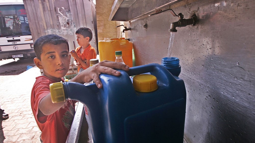 Palestinian child filling plastic water jug at an outdoor tap 