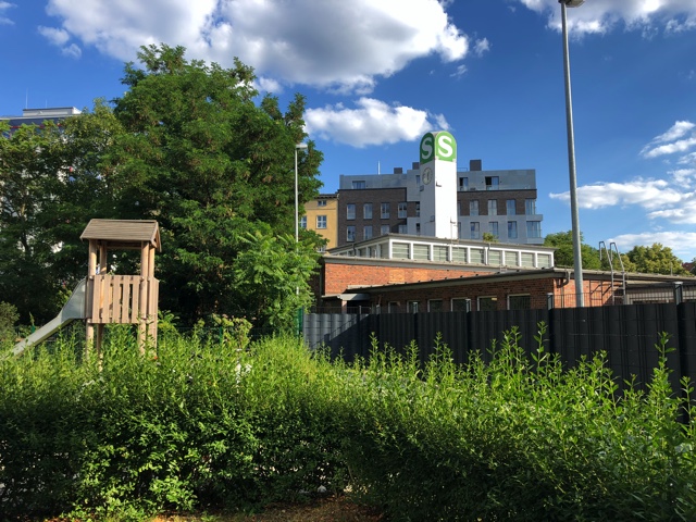 photo of tall grass with an industrial building in the background and a wooden building in the foreground