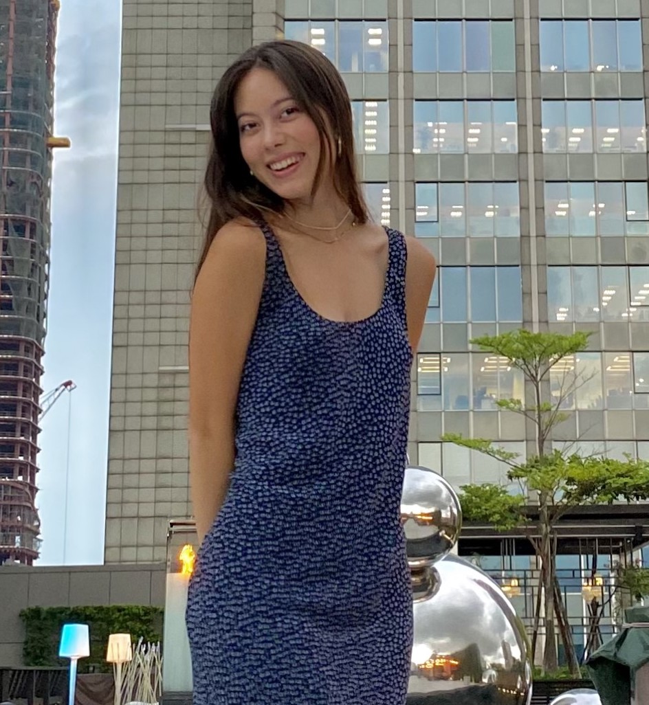 Lorraine stands outside in a city. She is smiling and wears a blue dress.