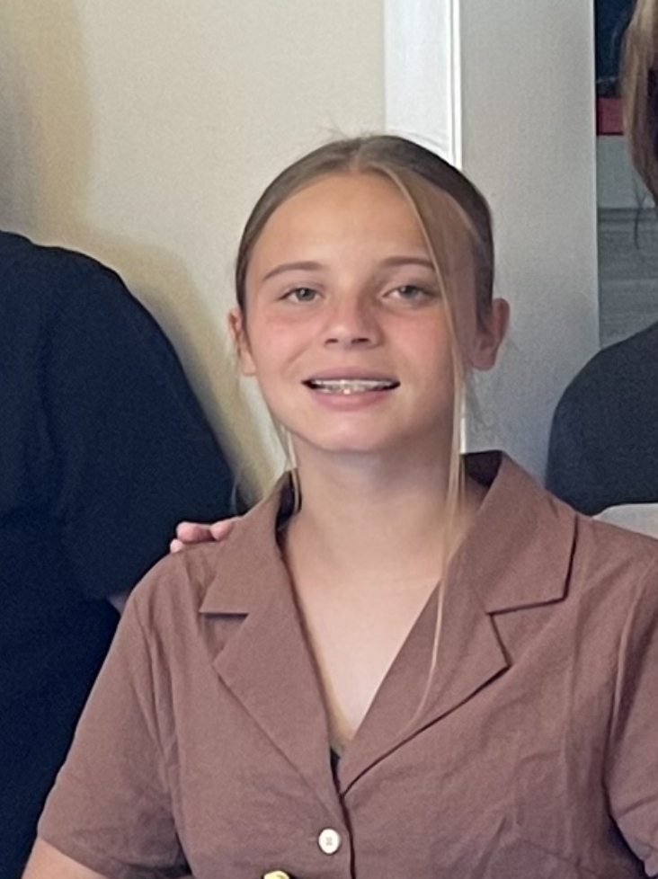 Isabella wears a brown button down shirt and smiles at the camera with her hair pulled back.