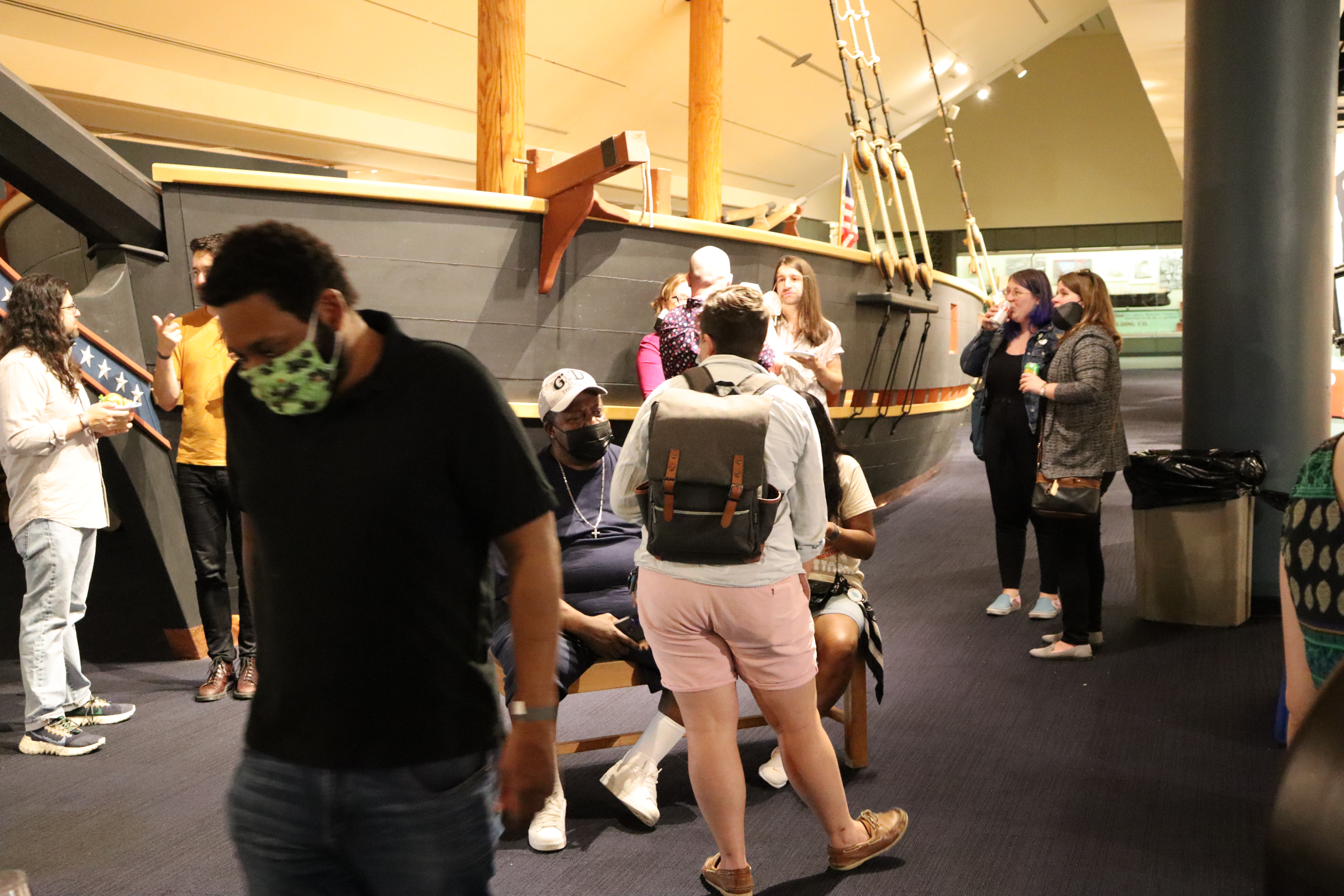 Visitors to a museum mingle in a gallery with a display of a historic boat.