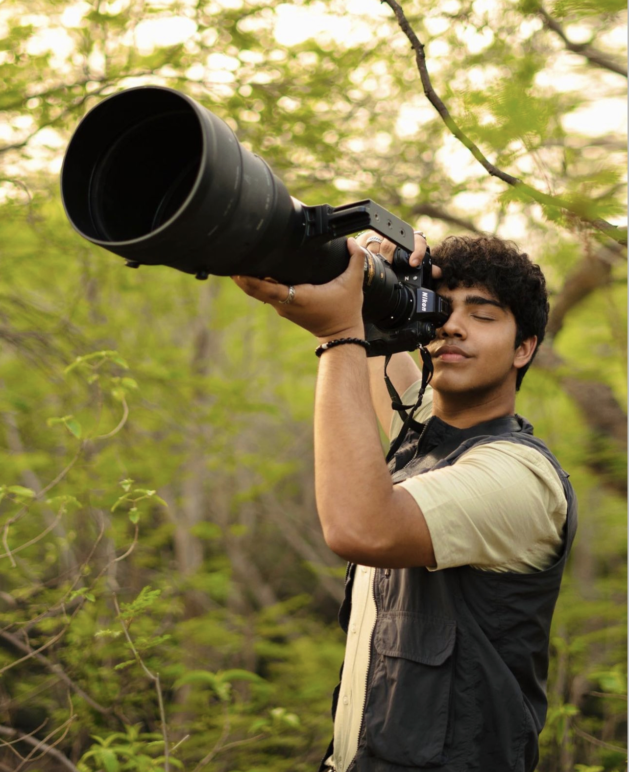 Aman Sharma holds a camera with a long lens surrounded by nature.