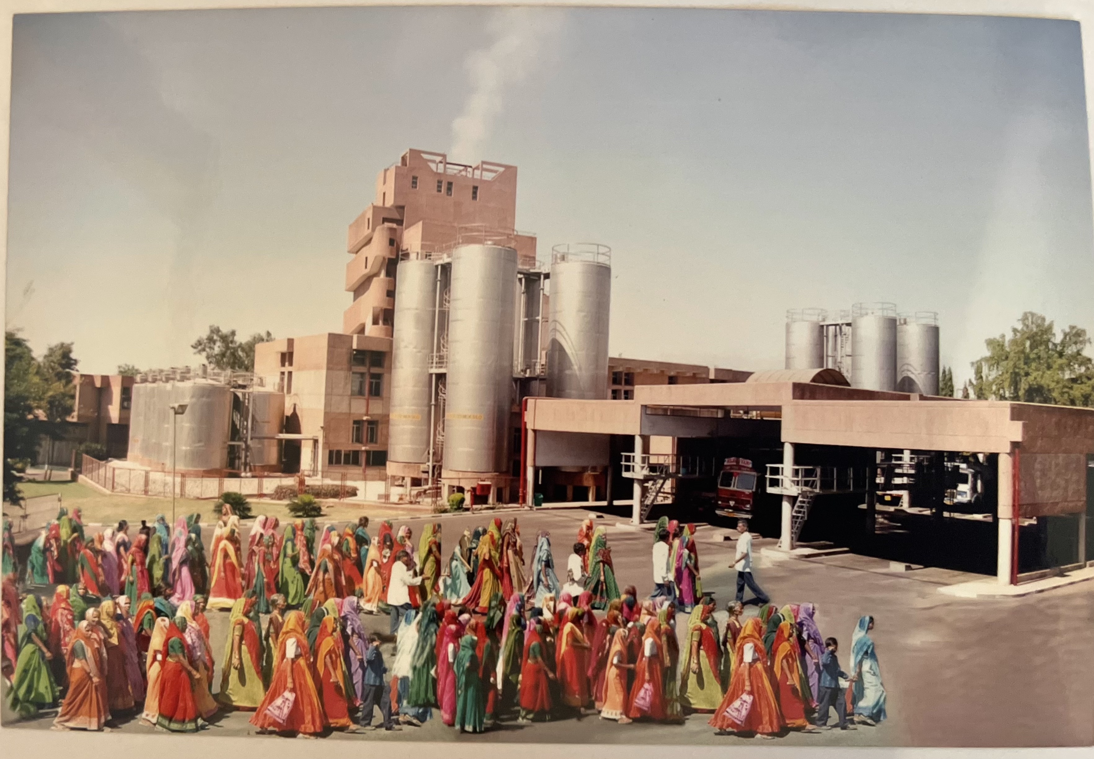 A vintage photo of women in colorful saris lined up in front of an industrial facility.