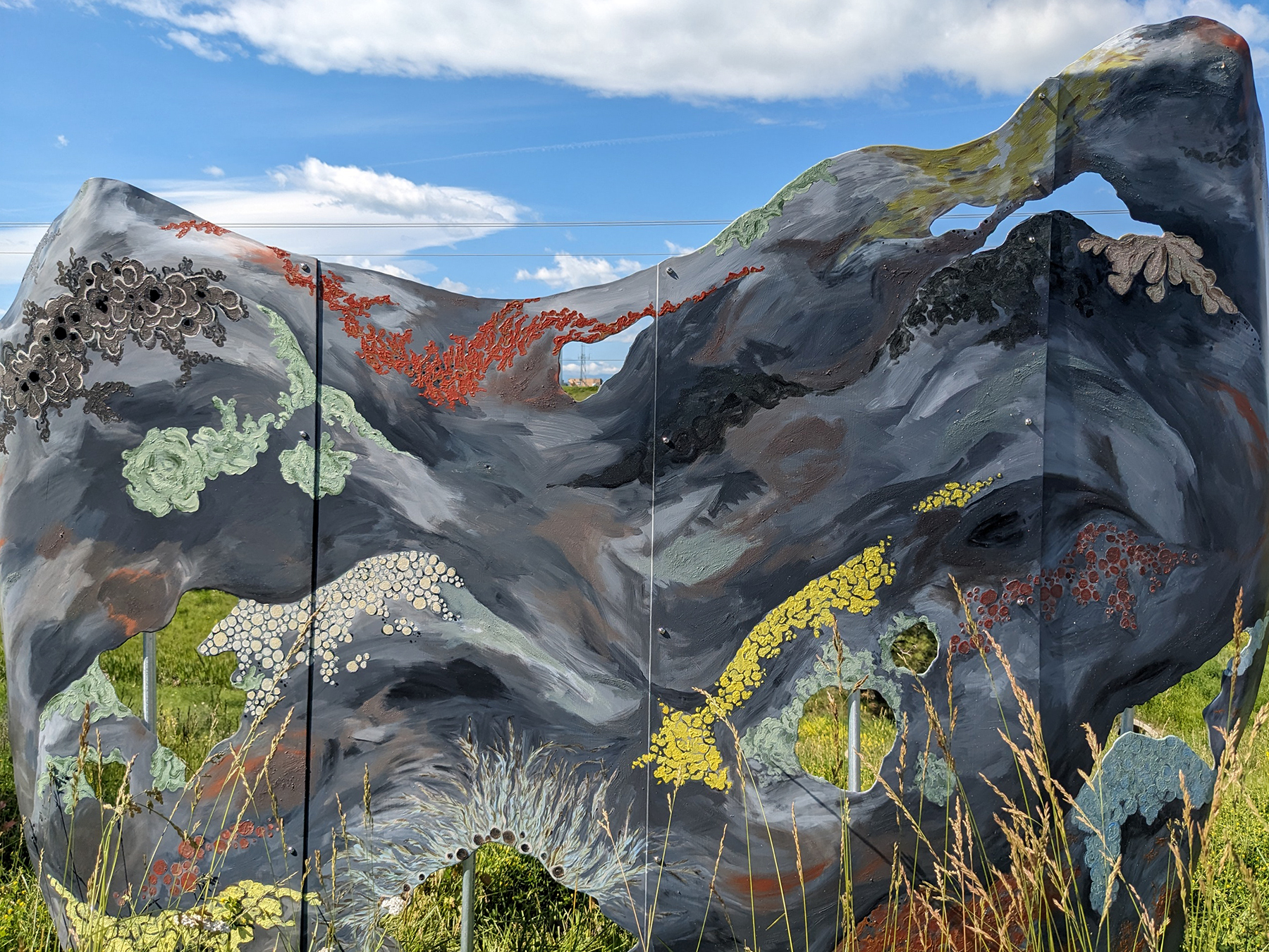 An art exhibition of a two dimensional representation of a mountain covered in various types of growth, displayed outdoors.