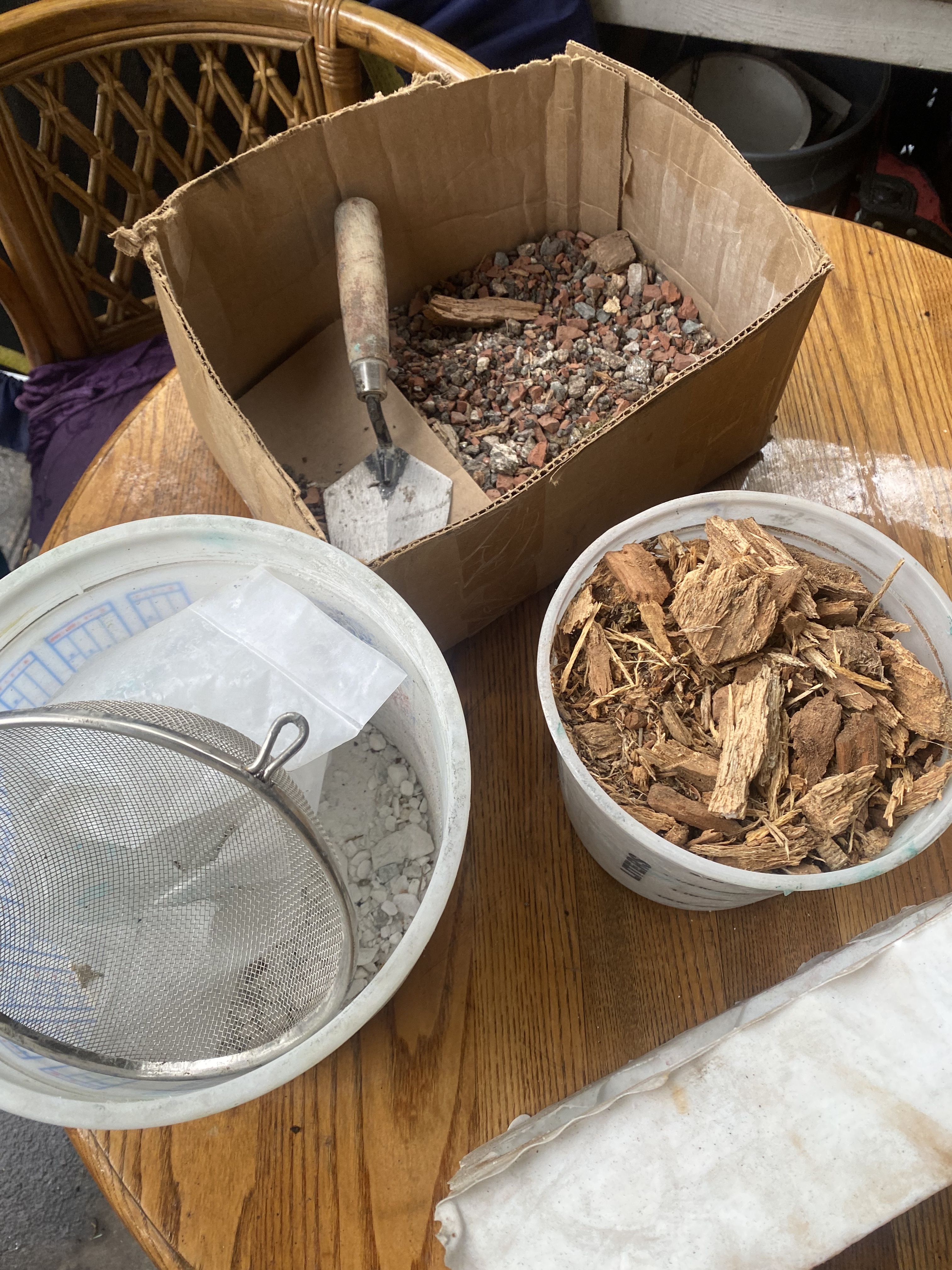 Containers of various organic materials including sand, wood chips, and pebbles.