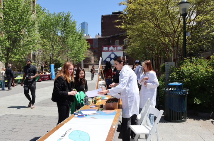 Two female students show off the activity at their booth at an Earth Week festival.