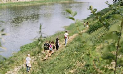 distant view of participants walking along the Arno river with vegetation in the foreground