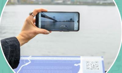 A hand holds up a phone to experience an AR animation of the Delaware River.