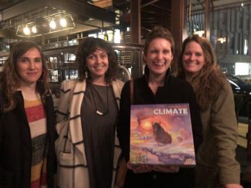 Members of Underwater New York stand next to each other in a dimly lit room, Nicole Miller holds a climate game in her arms