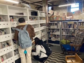 Two people stand with their back to the camera, looking at shelves of zines