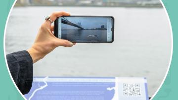 A hand holds up a phone to experience an AR animation of the Delaware River.